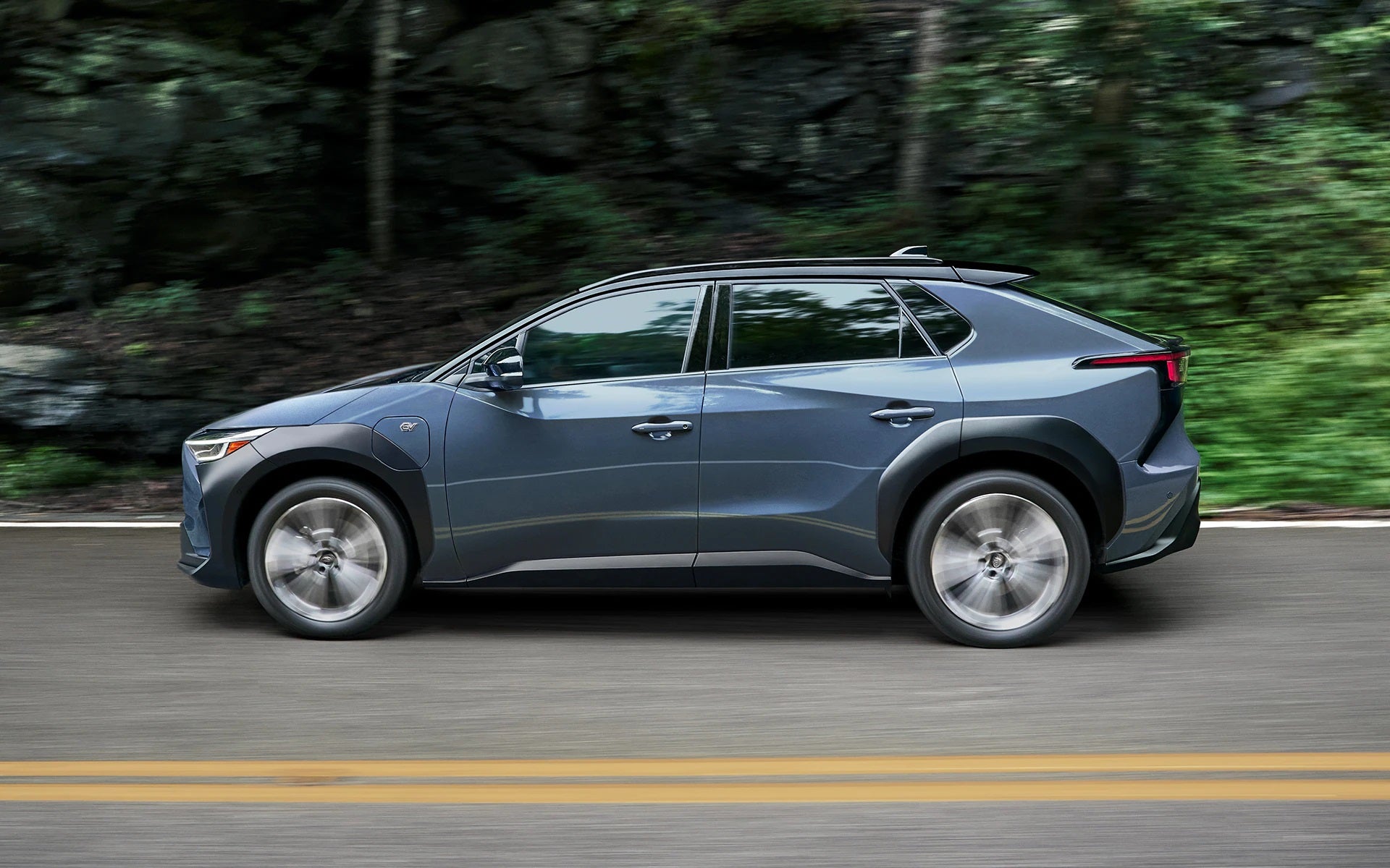 A SUV is moving on a road with backbround trees.
