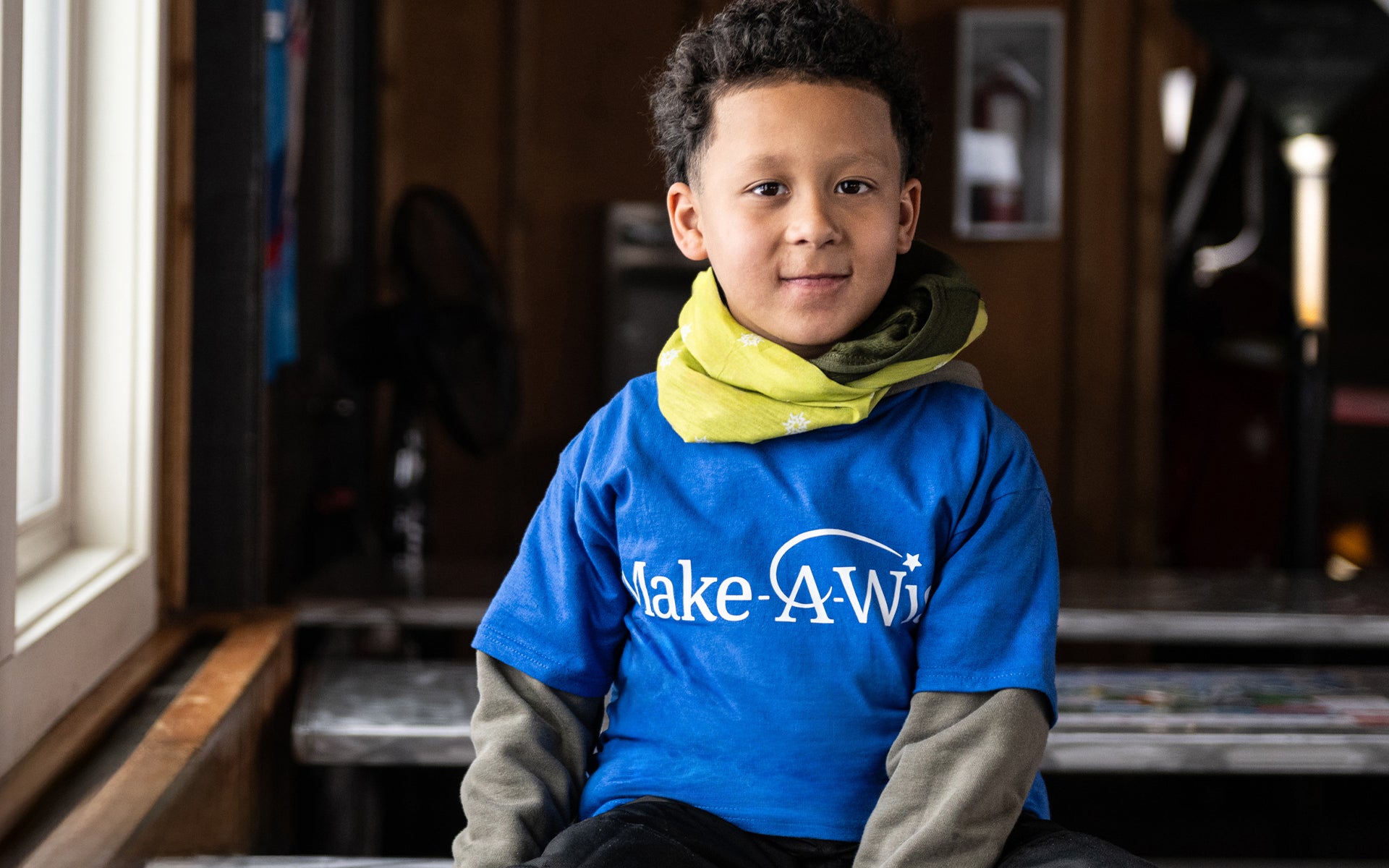 Make-A-Wish boy with bright scarf smiles at the camera.