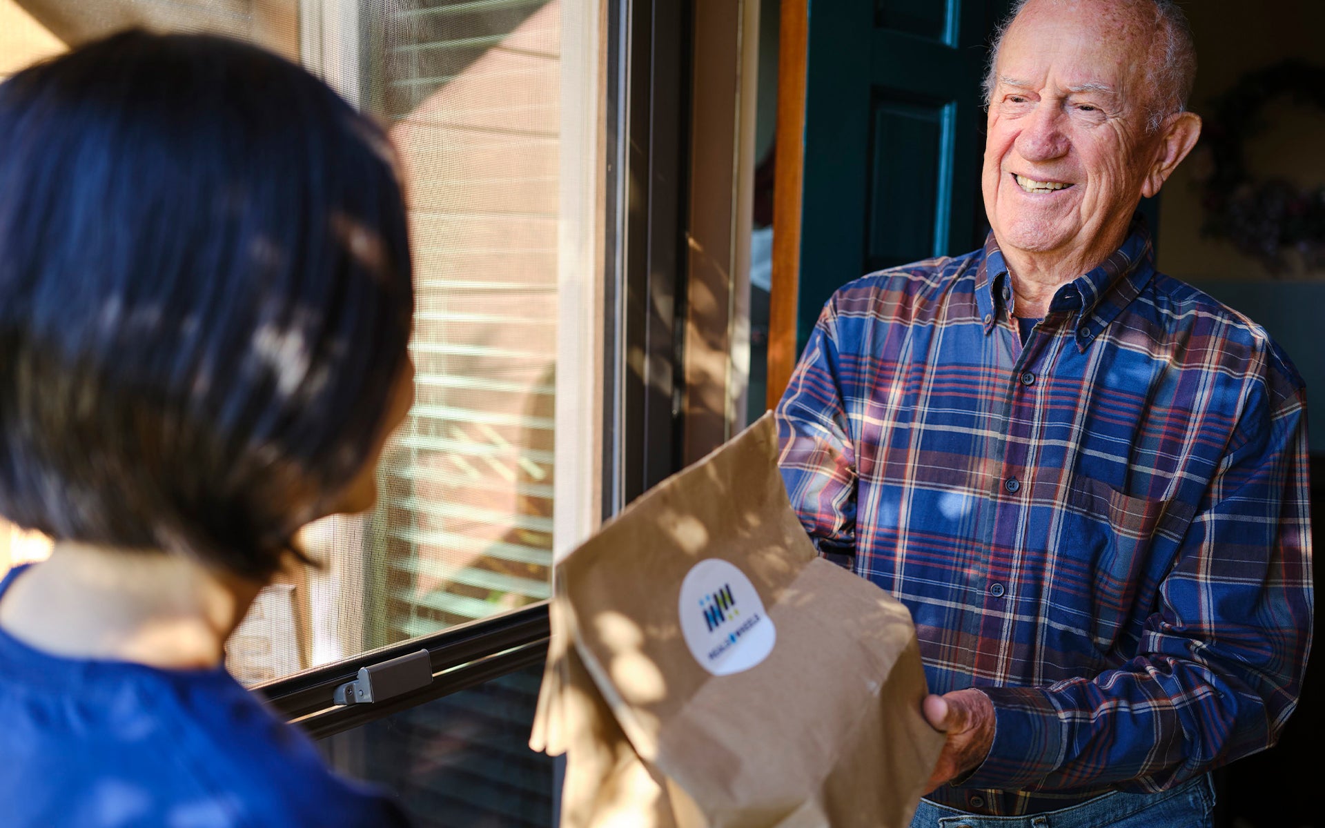 Smiling man receiving a Meals on Wheels delivery at his door