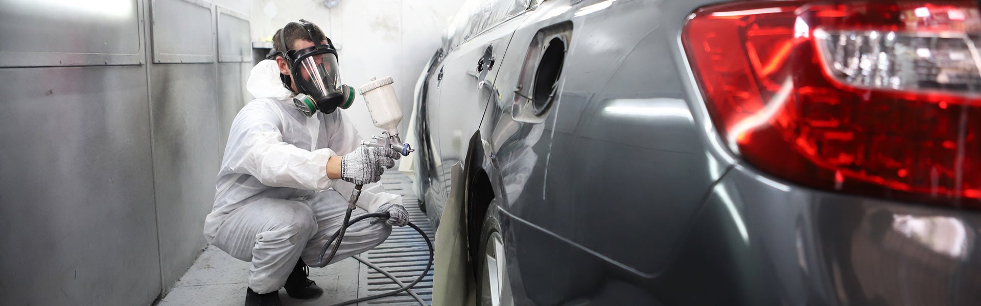 Painter in respirator spraying car in collision center.